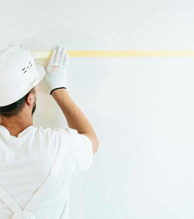 A construction worker applying tape on a wall in preparation for painting or measuring.